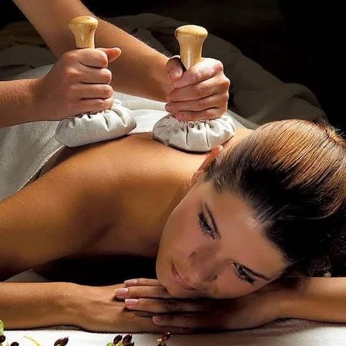 Two warm herbal potli bundles being pressed along a client's back during Potli massage